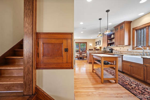 kitchen with light hardwood / wood-style floors, sink, hanging light fixtures, decorative backsplash, and stainless steel dishwasher