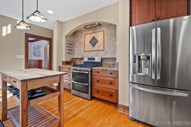 kitchen with appliances with stainless steel finishes, decorative backsplash, light stone countertops, pendant lighting, and light wood-type flooring