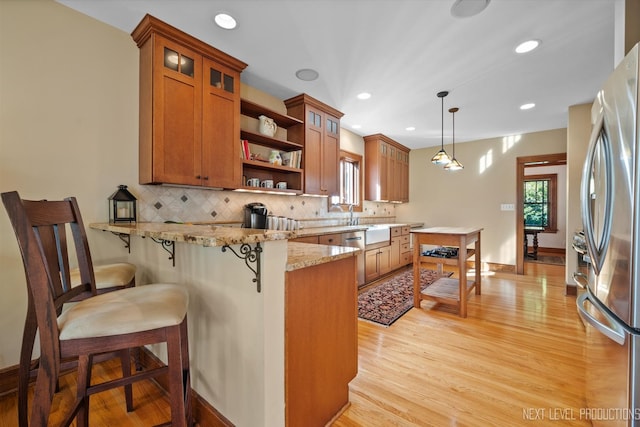 kitchen featuring a breakfast bar, light wood-type flooring, light stone counters, kitchen peninsula, and decorative light fixtures