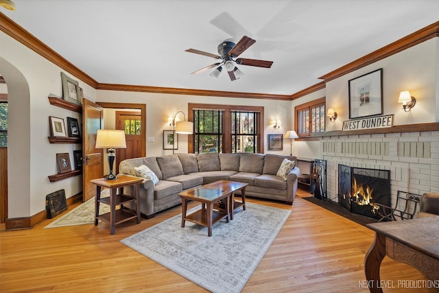 living room featuring ceiling fan, ornamental molding, a fireplace, and light hardwood / wood-style floors