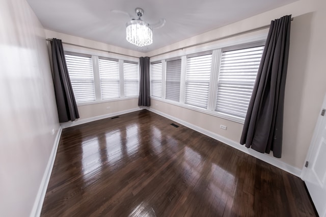 spare room with a notable chandelier and dark hardwood / wood-style flooring