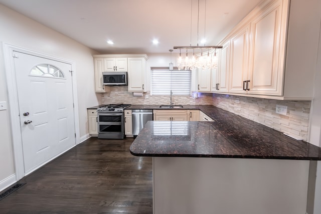 kitchen featuring kitchen peninsula, dark stone countertops, stainless steel appliances, sink, and decorative light fixtures