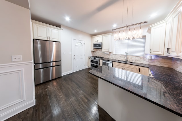 kitchen featuring appliances with stainless steel finishes, sink, kitchen peninsula, decorative light fixtures, and dark hardwood / wood-style floors