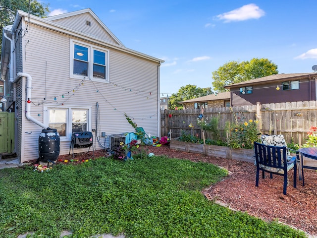 rear view of house with central AC unit and a yard