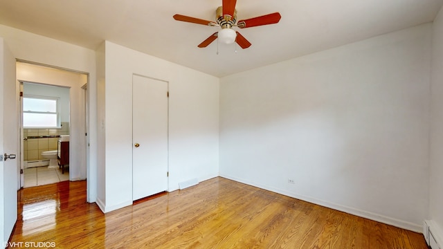 unfurnished bedroom with a baseboard heating unit, light wood-type flooring, a closet, and ceiling fan