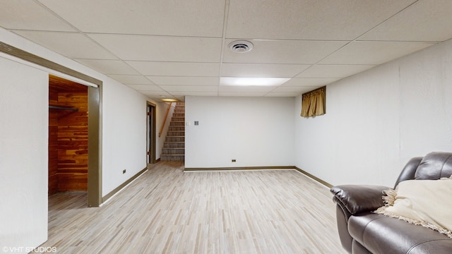 unfurnished room with light wood-type flooring, a drop ceiling, and wooden walls