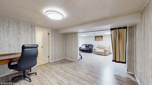 office area with a textured ceiling, wood walls, and light hardwood / wood-style floors