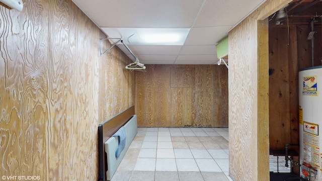 basement with gas water heater, wooden walls, a paneled ceiling, and light tile patterned floors