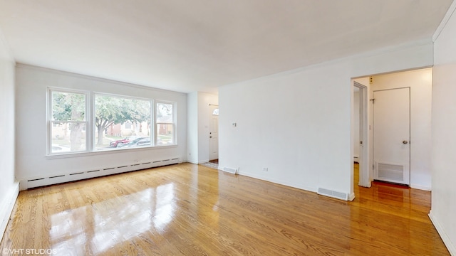 empty room featuring ornamental molding, a baseboard heating unit, and light wood-type flooring