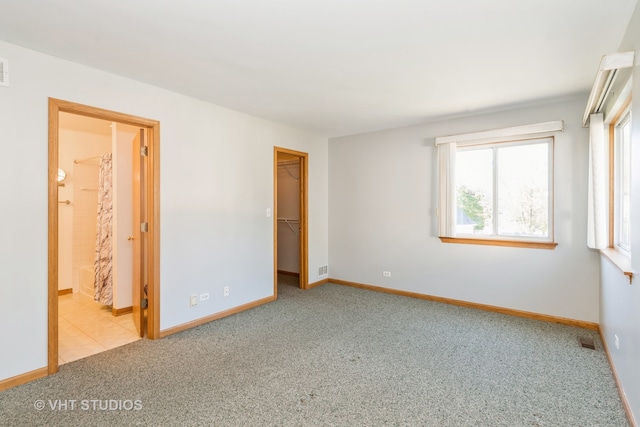 unfurnished bedroom with a closet, light colored carpet, a walk in closet, and connected bathroom