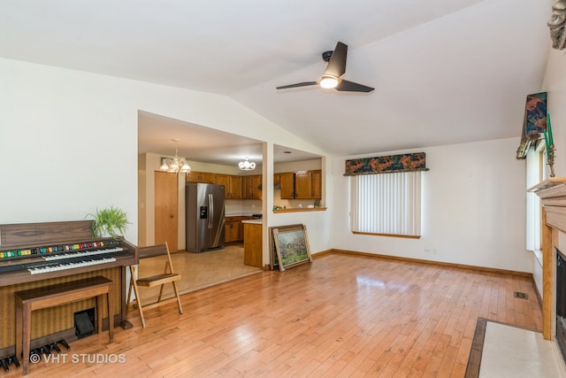 living room with ceiling fan with notable chandelier, lofted ceiling, and light hardwood / wood-style flooring