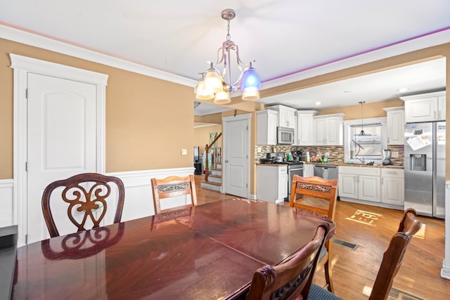 4035 W Marquette Rd, Chicago, IL 60629 - dining space featuring a chandelier, stairs, wainscoting, light wood-type flooring, and crown molding