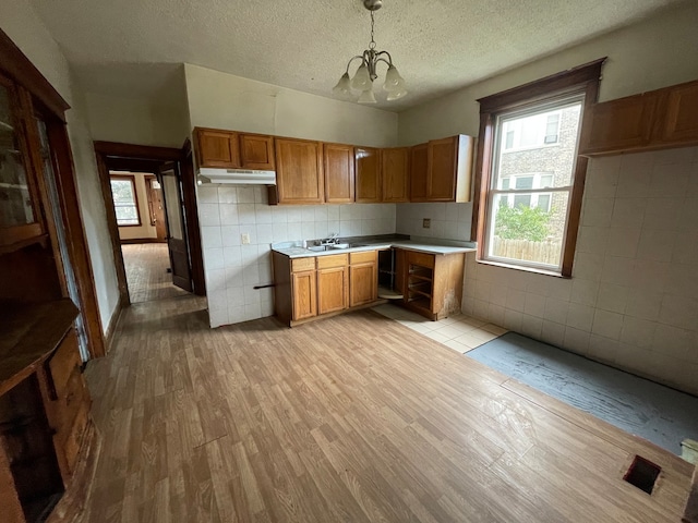 kitchen with tile walls, a textured ceiling, hanging light fixtures, light hardwood / wood-style flooring, and an inviting chandelier