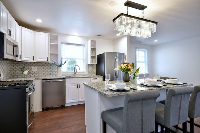 kitchen with sink, appliances with stainless steel finishes, white cabinetry, a kitchen island, and decorative backsplash