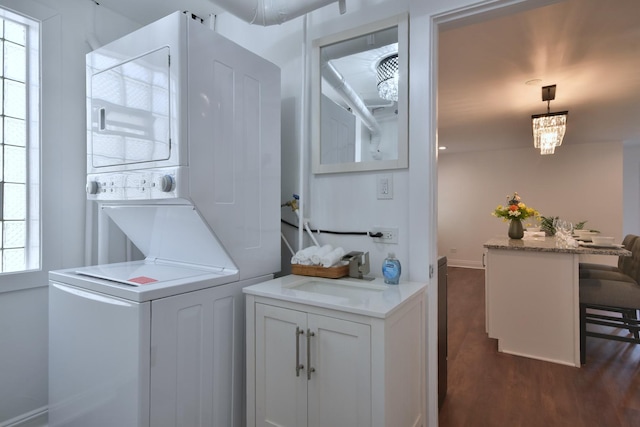 laundry room featuring a healthy amount of sunlight, stacked washer / dryer, dark hardwood / wood-style flooring, and sink