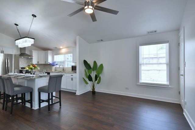 kitchen featuring lofted ceiling, wall chimney exhaust hood, decorative light fixtures, white cabinets, and backsplash