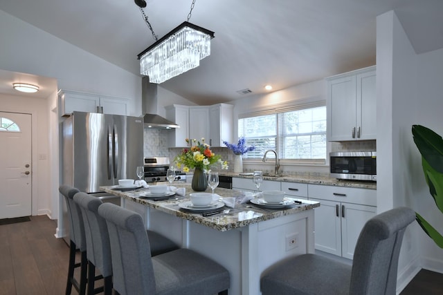 kitchen with white cabinetry, stainless steel appliances, sink, and wall chimney range hood