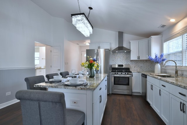 kitchen with wall chimney exhaust hood, sink, hanging light fixtures, stainless steel appliances, and white cabinets