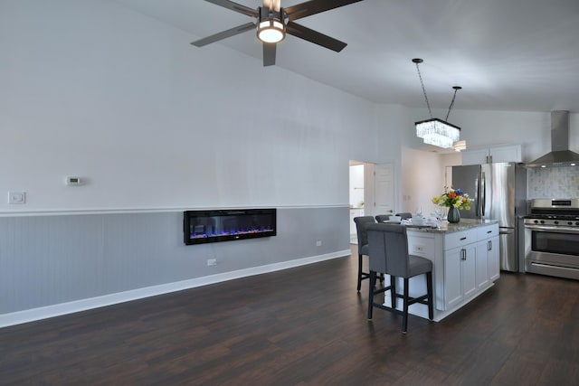 kitchen with a kitchen island, appliances with stainless steel finishes, white cabinets, light stone countertops, and wall chimney exhaust hood