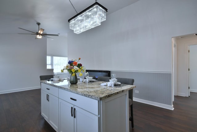 kitchen featuring white cabinets, dark hardwood / wood-style flooring, a center island, ceiling fan, and light stone countertops