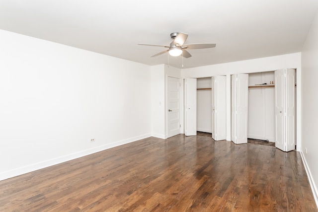 unfurnished bedroom featuring dark wood-type flooring, ceiling fan, and two closets