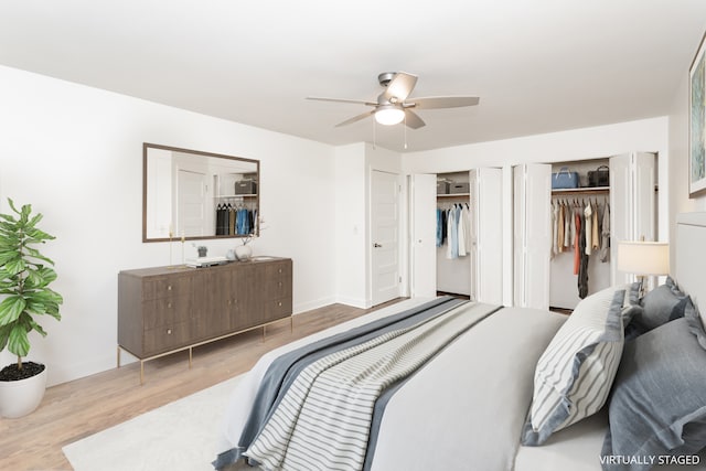 bedroom featuring ceiling fan, light hardwood / wood-style flooring, and two closets