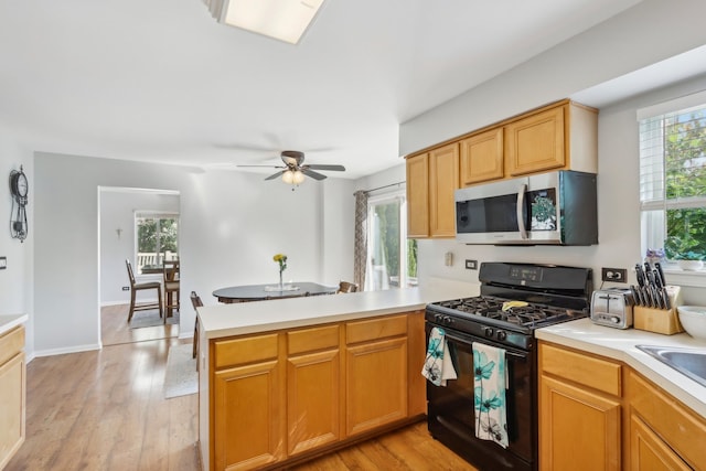 kitchen with light wood-type flooring, kitchen peninsula, ceiling fan, and black gas range