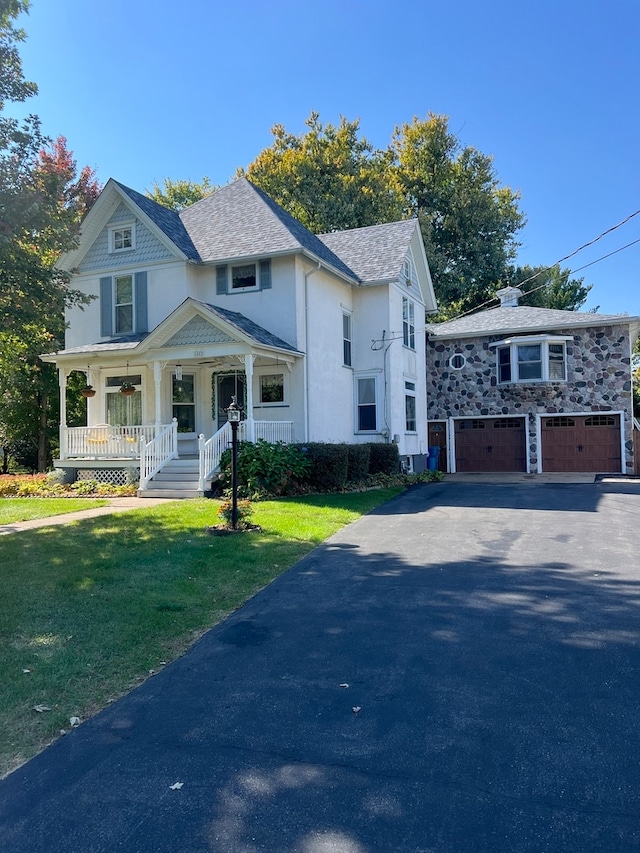 view of front of property featuring covered porch, a garage, and a front lawn