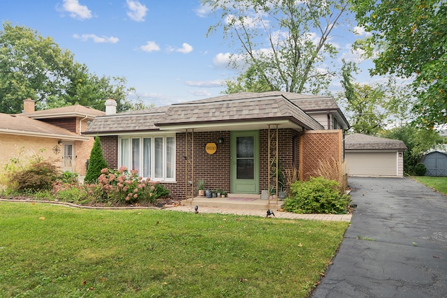 single story home with covered porch, a front lawn, an outbuilding, and a garage