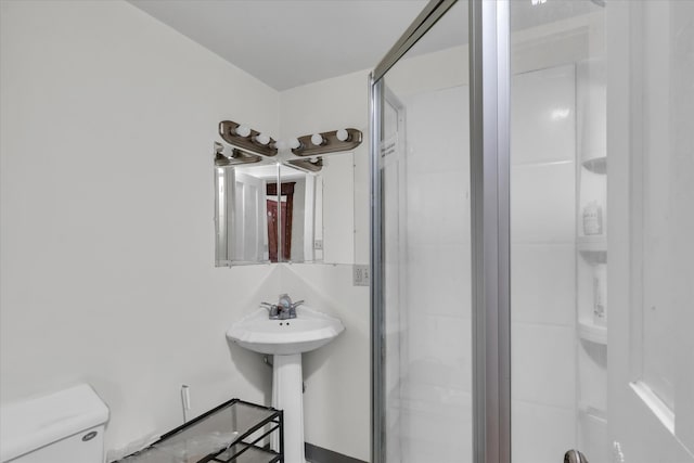 bathroom featuring a shower with door, toilet, and sink