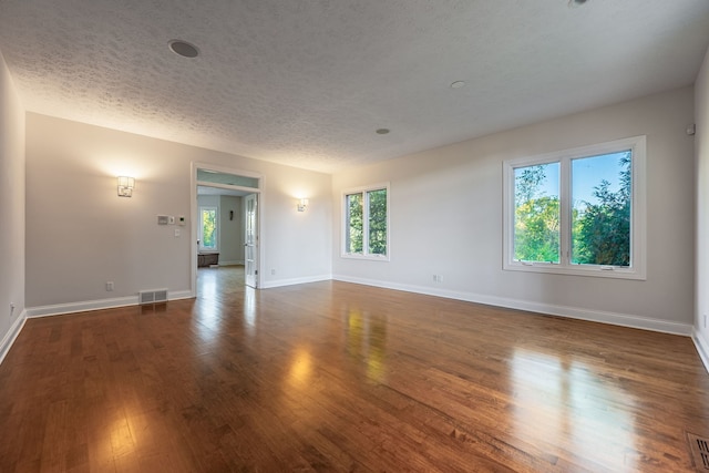 empty room with a textured ceiling, dark hardwood / wood-style flooring, and a wealth of natural light