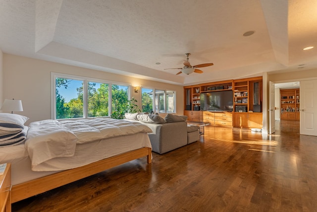 bedroom featuring ceiling fan, a textured ceiling, a tray ceiling, and dark wood-type flooring