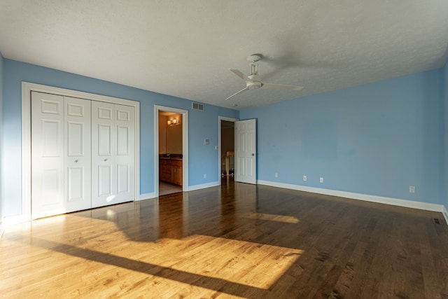 unfurnished bedroom with ceiling fan, hardwood / wood-style flooring, ensuite bathroom, and a textured ceiling