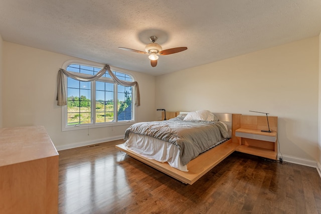 bedroom with a textured ceiling, dark wood-type flooring, and ceiling fan