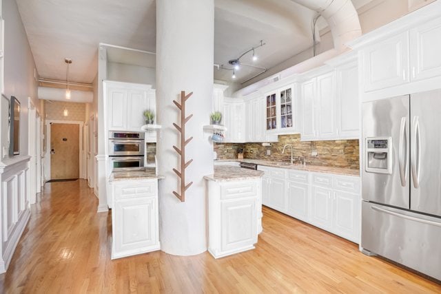 kitchen with white cabinets, appliances with stainless steel finishes, light wood-type flooring, and tasteful backsplash