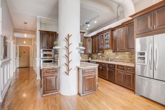 kitchen featuring light wood-type flooring, tasteful backsplash, decorative light fixtures, stainless steel appliances, and light stone countertops