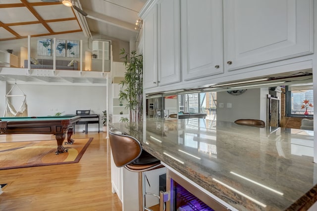 interior space featuring vaulted ceiling with beams, white cabinets, dark stone countertops, billiards, and light hardwood / wood-style floors