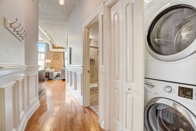 laundry room with stacked washer and clothes dryer and light hardwood / wood-style flooring