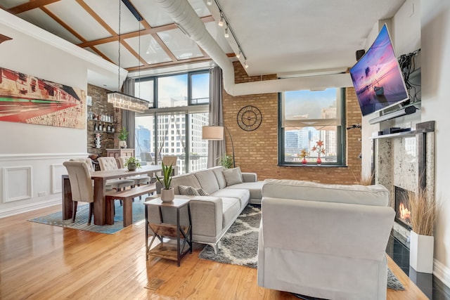 living room featuring vaulted ceiling with beams, brick wall, wood-type flooring, rail lighting, and a fireplace