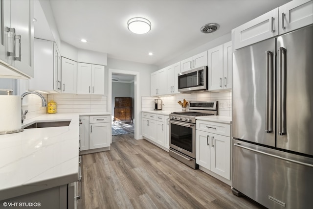 kitchen with appliances with stainless steel finishes, light hardwood / wood-style floors, white cabinetry, light stone countertops, and sink