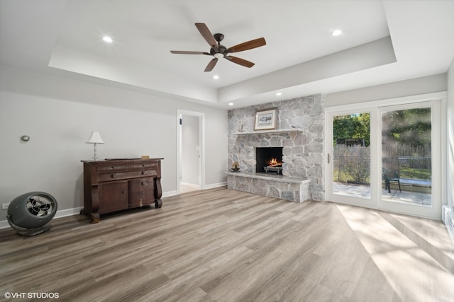 unfurnished living room with light hardwood / wood-style floors, a raised ceiling, a stone fireplace, and ceiling fan