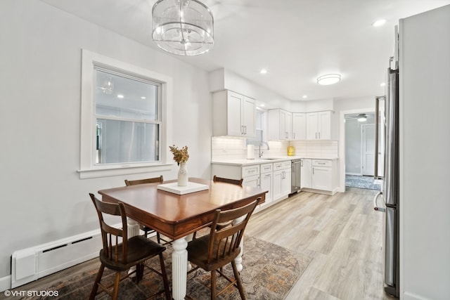 dining area featuring a baseboard radiator, light hardwood / wood-style floors, ceiling fan with notable chandelier, and sink