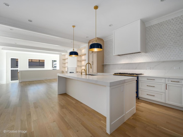 kitchen with pendant lighting, white cabinetry, sink, backsplash, and a kitchen island with sink