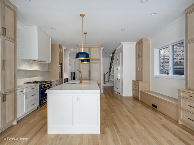 kitchen with tasteful backsplash, sink, hanging light fixtures, high end appliances, and a kitchen island with sink