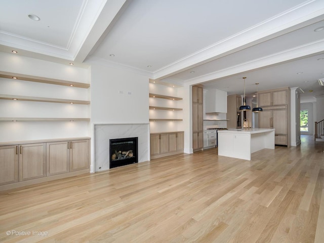 unfurnished living room with built in features, sink, crown molding, a premium fireplace, and light wood-type flooring