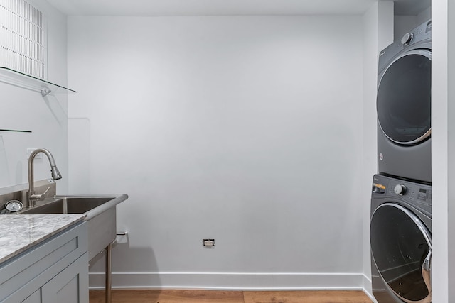 clothes washing area with stacked washer and clothes dryer, light hardwood / wood-style floors, sink, and cabinets