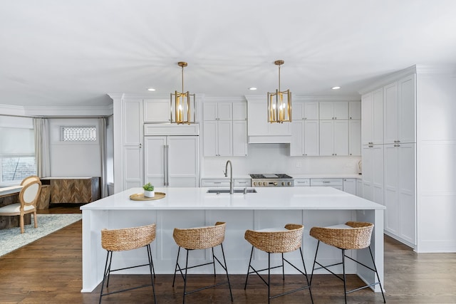 kitchen with sink, an island with sink, stainless steel stove, paneled built in fridge, and hanging light fixtures