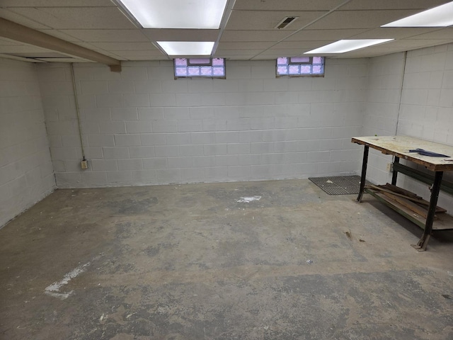 basement featuring visible vents, a drop ceiling, and concrete block wall