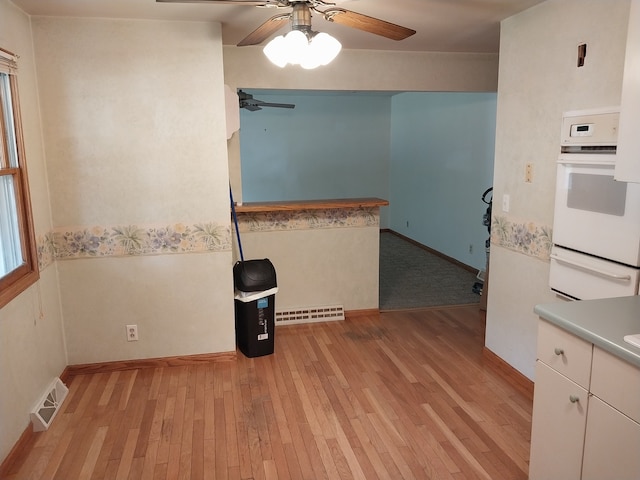 kitchen with light wood-type flooring, oven, ceiling fan, and white cabinets