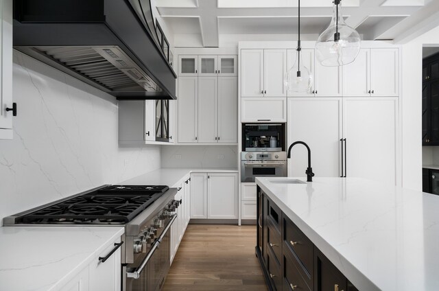 kitchen with appliances with stainless steel finishes, white cabinetry, light stone countertops, decorative light fixtures, and premium range hood